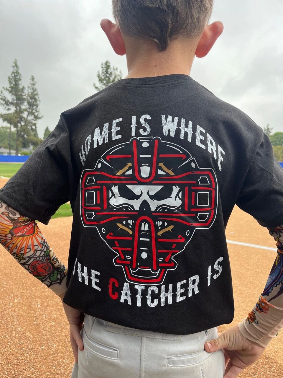 Back of the black Home Is Where The Catcher Is tee on a young player